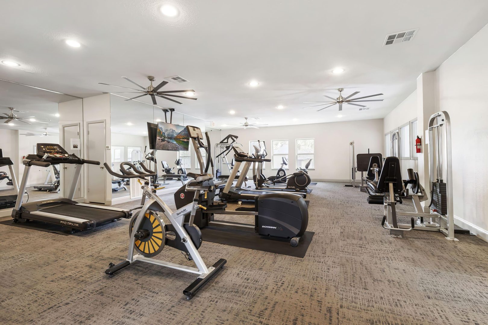 a gym room with treadmills, exercise equipment and ceiling fans at The  Adelene